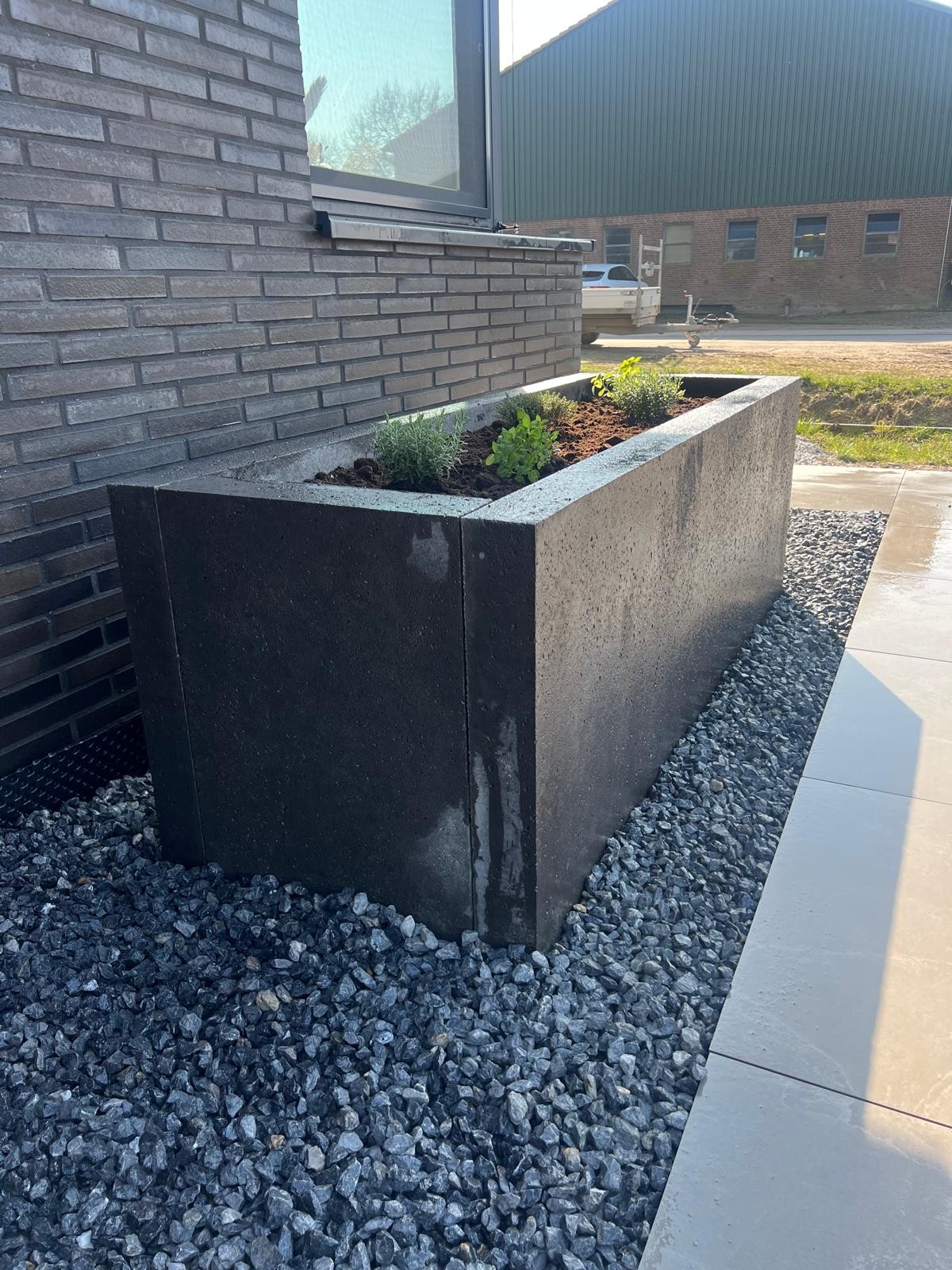 Hochbeet aus dunklen Betonelementen mit Kräutern im Kiesbett